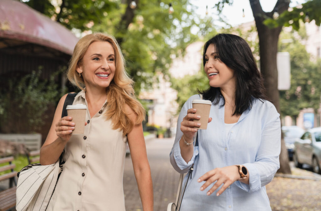 A female caregiver walks with her friend and drinks hot beverages outdoors in a city park to relax and enjoy.