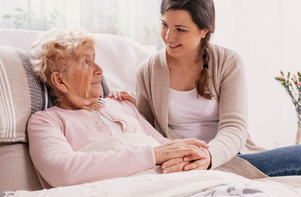 A female caregiver sitting beside a senior woman with Alzheimer's trying to comfort her while holding her hand.