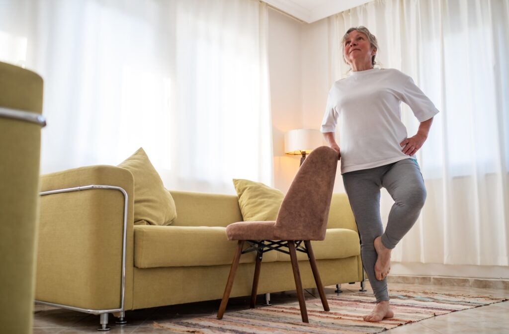 an older woman performing balance exercise by standing on one leg and holding a chair for support.