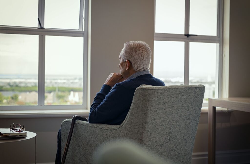 A senior sitting in an armchair gazes forlornly out the window due to mood changes from living alone